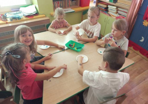 Dzieci przy stolikach przyklejają kuleczki w plasteliny.